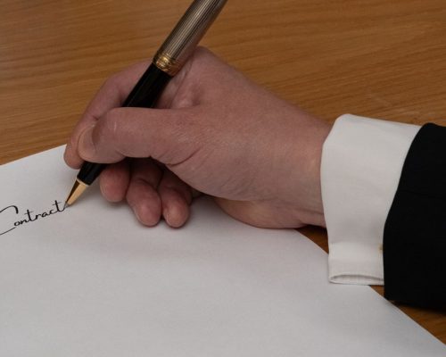 A professional signing a business contract with a fountain pen on a wooden desk.